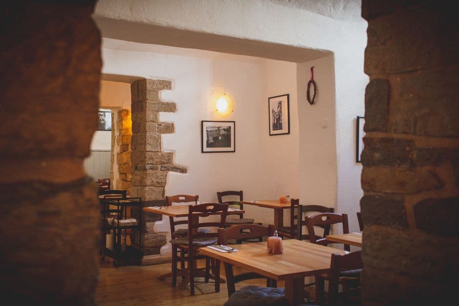 Warm, modern restaurant dining room with natural wood tables, soft overhead lighting, and a few guests sharing a meal in relaxed conversation — feels inviting and unhurried
