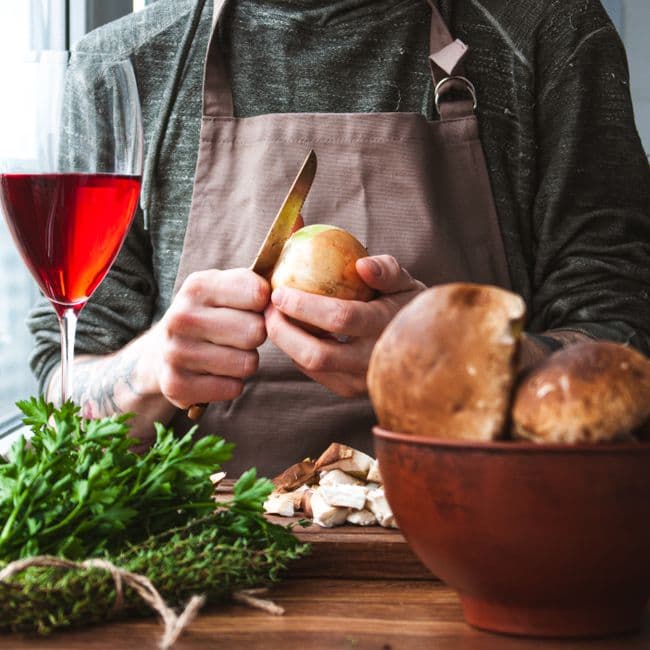A chef in a clean kitchen pressing herbs into a pan, focused and calm — the kind of cooking that is practiced and deliberate, not rushed
